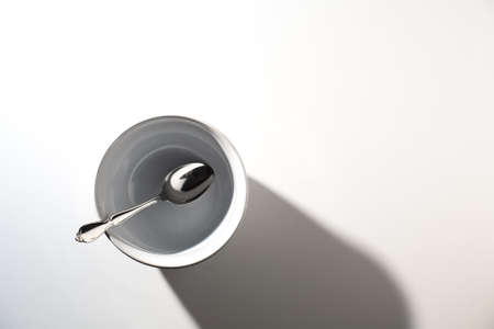 Empty White Bowl with Spoon on a White Background and Shadowsの写真素材