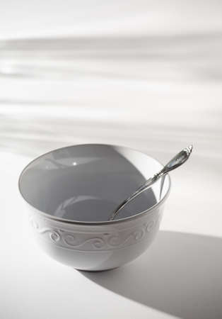 Empty White Bowl with Spoon on a White Background and Shadowsの写真素材