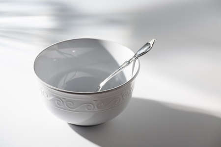 Empty White Bowl with Spoon on a White Background and Shadowsの写真素材