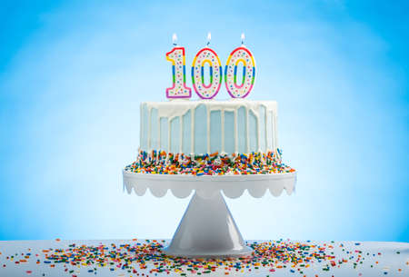Blue Birthday Cake with Sprinkles on a White Cake Plate and Blue Background with 100 candles on Topの写真素材