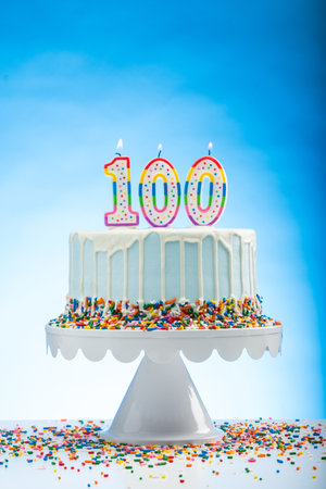 Blue Birthday Cake with Sprinkles on a White Cake Plate and Blue Background with 100 candles on Top