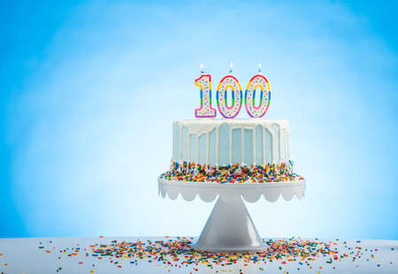 Blue Birthday Cake with Sprinkles on a White Cake Plate and Blue Background with 100 candles on Topの写真素材
