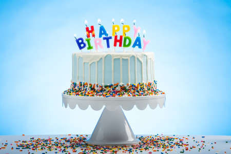 Blue Birthday Cake with Sprinkles on a White Cake Plate and Blue Background with Happy Birthday candles on Topの写真素材
