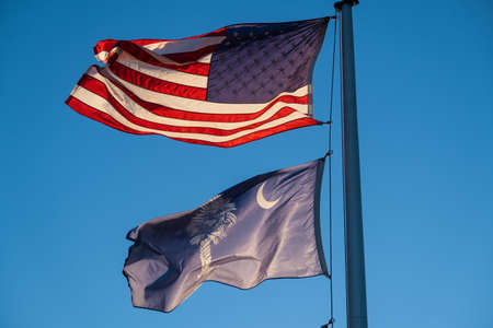 A United States and South Carolina Flag Blowing in the Wind with the Sun Shinning Behind Themの写真素材
