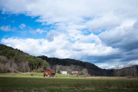 Red Barn in a Large Field with Mountain Surrounding It.の写真素材
