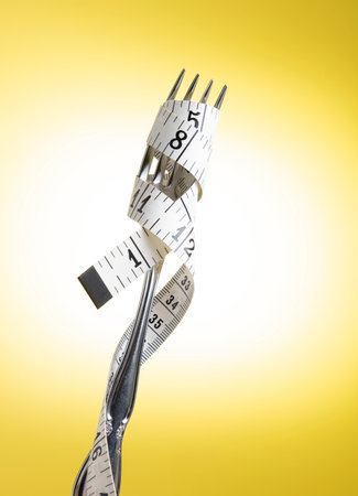 Silver Fork with Measuring Tape Wrapped Aroung It on a Yellow Backgroundの写真素材