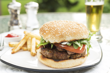 Bacon and Bleu Stuffed Cheeseburger topped with arugula tomato on a toatsed sesame seed bun served with fries ketchup and beerの写真素材