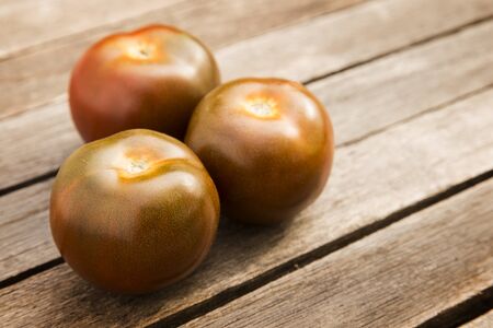 three fresh kumato or brown tomatoes on wood planksの写真素材