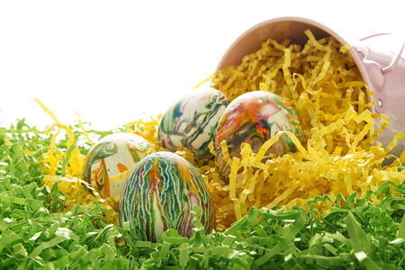 tie-dyed easter eggs in a pink bucket with green and yellow paper grassの写真素材