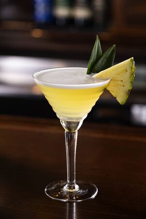 a Pineapple Martini with fresh fruit garnish sits on a wood bar topの写真素材