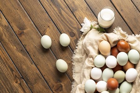 basket of fresh natural organice blue, green, brown and white eggs on wood background with bottle of milk, overheadの写真素材