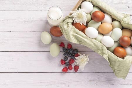 basket of fresh natural organice blue, green, brown and white eggs on wood background with bottle of...