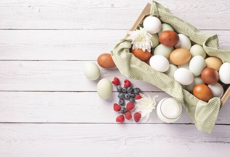 basket of fresh natural organice blue, green, brown and white eggs on wood background with bottle of milk, overheadの写真素材