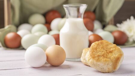 basket of fresh natural organice blue, green, brown and white eggs on wood background with fresh basked biscuits and milkの写真素材