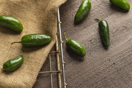 fresh jalapeno peppers on a burlap sack in a wire basket on a wood background.の写真素材