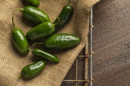 fresh jalapeno peppers on a burlap sack in a wire basket on a wood background.の写真素材