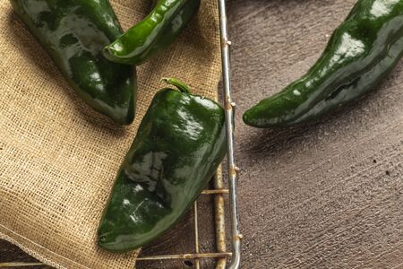 fresh poblano peppers on a burlap sack in a wire basket on a wood background.の写真素材
