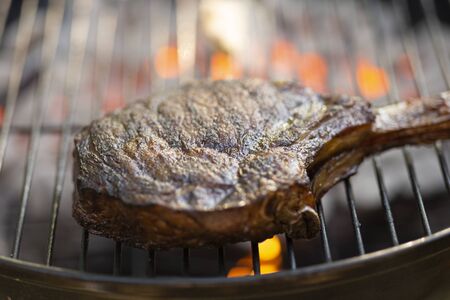 a bone-in tomahawk ribeye steak cooking on grill with flames, angled view