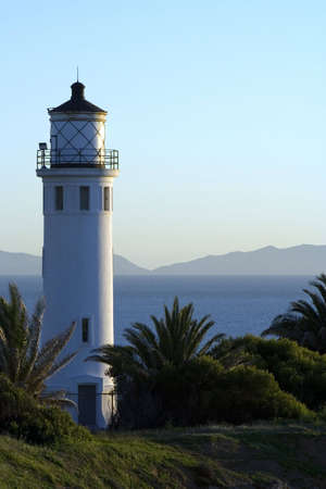 lighthouse overlooking blue ocean and mountains in the distanceの写真素材