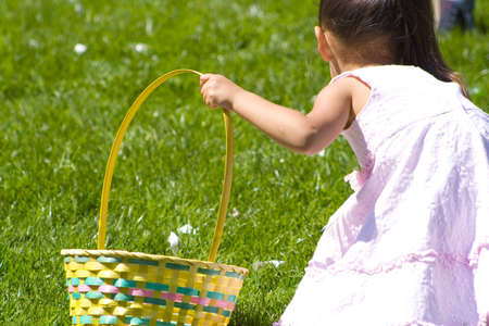 young girl reaches down for an easter egg while holding basketの写真素材
