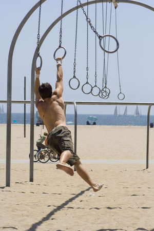 male gymnast swings from the rings at the beach