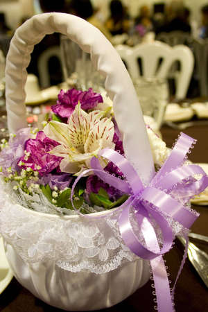 spring flowers in a white cloth basket with lavender ribbon at a weddingの写真素材