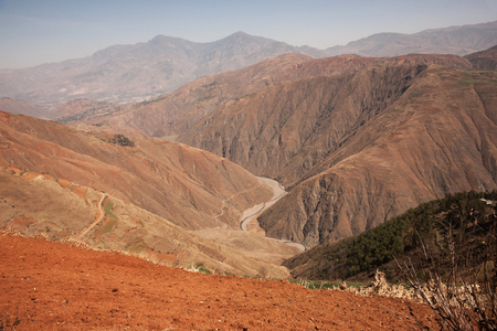 Small road placed between mountains of brown sand and dirt to travel from one side of the mountain to the other in the afternoon, Chinaの写真素材