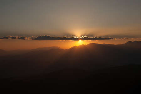 Sun setting behind the clouds and a silhouette of mountains at nightfall in China.の写真素材
