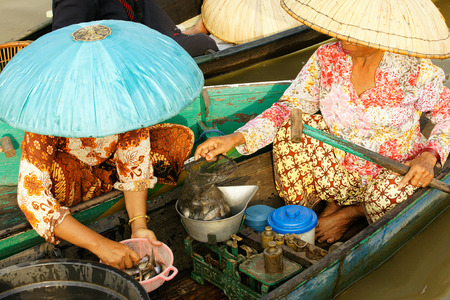 Two asian women at daytime weighing and selling fresh fish in a boat on a floating market just to make a living.の写真素材