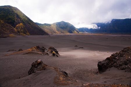 Sand sea with mountains at the background and a clouded sky in the morning at the Tengger Semeru National Park in East Java, Indonesia.の写真素材