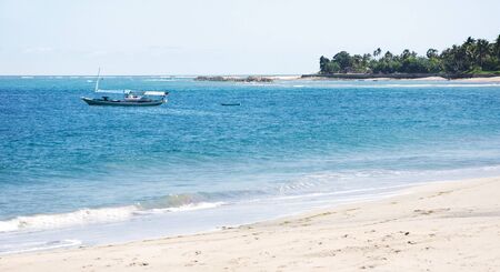 Empty boat at a white sand beach and clear blue ocean waves at Flores.の写真素材