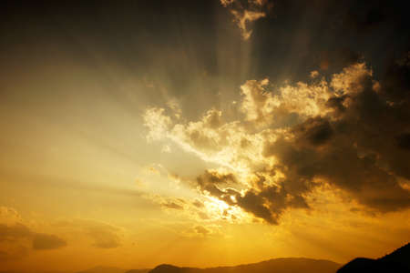 Sun setting behind the clouds and a silhouette of mountains at nightfall in China.