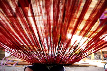 Woman weaving red threads with hands on weaving device seen from a low angle view in Flores Samosir.の写真素材