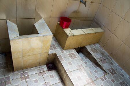 Asian tiled bathroom and red bucket to fill with water and wash yourself with.の写真素材
