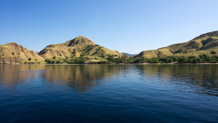 Coastline of mountains with green vegetation reflected  in blue ocean water at Labuan Bajo in Flores, Indonesia.の写真素材