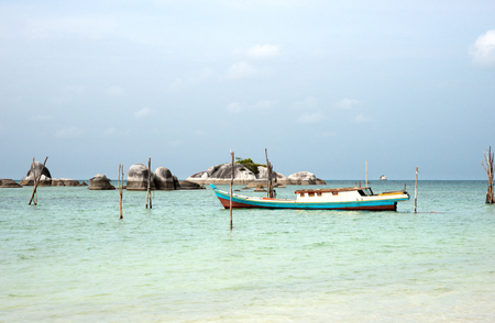 Empty fishing boat docked at the turquoise colored ocean coast near white sand beach in the afternoon with rocks on the ocean horizon in Belitung, Indonesia
の写真素材