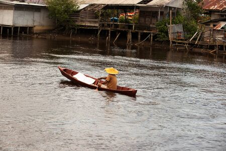 One asian man rowing his little boat with a small paddle on a brown colored riverbank in the afternoon, Singkawang.の写真素材