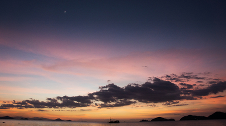 Boat silhouette crossing the ocean at nightfall with orange violet purple blue colored sunset sky on the horizon, Labuan Bajo Bajawa.の写真素材
