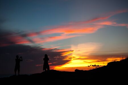 The silhouette man and girl on a cliff above the sea and watching the sunset