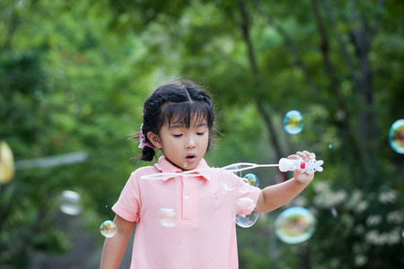 Portrait of funny asian little girl is blowing soap bubbles