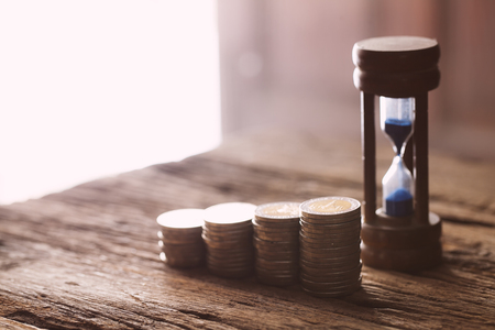 The coins on the table in front of the  hourglassの写真素材