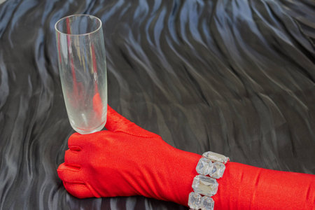 Hand with a red glove and necklace holding a cup on dark backgroundの写真素材