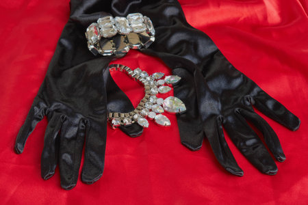 two pretty black gloves next to shiny necklace and bracelet on red backgroundの写真素材