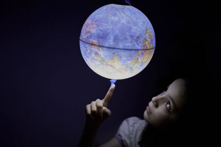 Little girl looking interested in the dark at an illuminated earth globeの写真素材