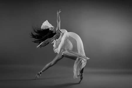 Young pregnant ballerina performing classical ballet pose with silk cloth in studio in black and whiteの写真素材