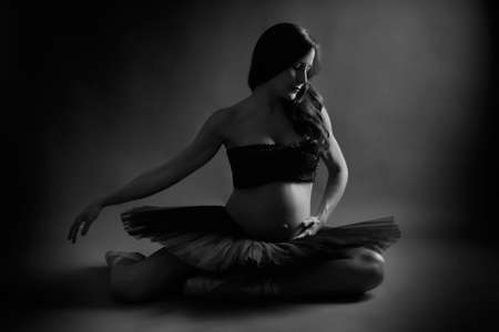 Young pregnant ballerina performing classical ballet pose with black top and tutu in studioの写真素材