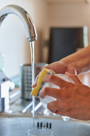 Hands scrubbing glass cup with sponge and detergent in kitchenの写真素材