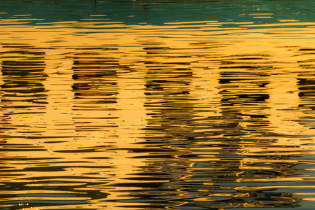 Reflection of windows in the waters of lake created by the light of the setting sun forming different size and shape of glimmer and colorsの写真素材