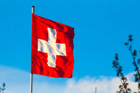 Swiss Confederation, Switzerland national flag waving on blue sky backgroundの写真素材
