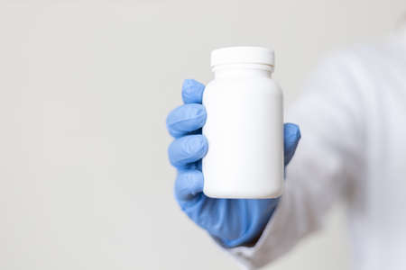 Hand in a Lab Coat and a blue medical glove holding a white pill bottleの写真素材